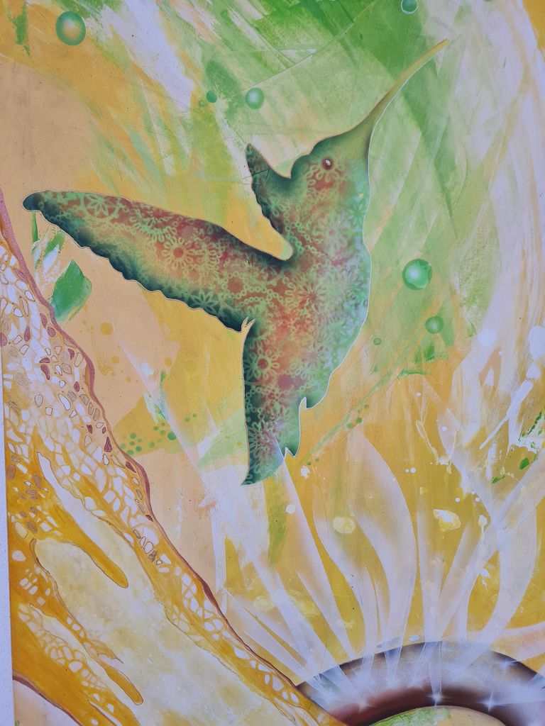 Bunte Graffiti-Darstellung eines Kolibris mit floralen Mustern, umgeben von grünen und gelben abstrakten Formen.